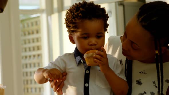 Front view of cute little black son eating cupcake in kitchen of comfortable home 4k