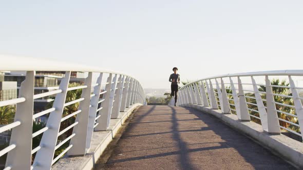 Fit african american man exercising outdoors in city, running on footbridge