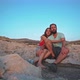 Young couple seating on a rocky hill and hugging while staring at the sunset - VideoHive Item for Sale