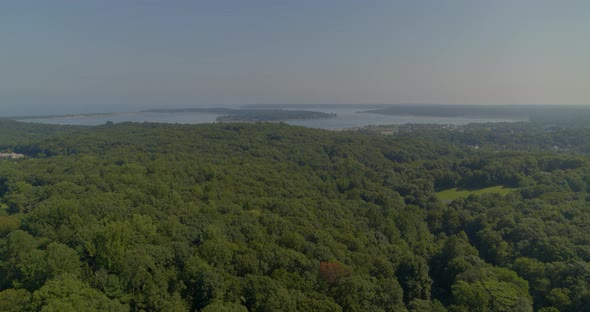 Flying Over Dense Forest Trees and Towards Bay on a Sunny Day in Long Island