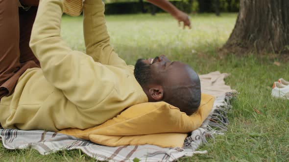 Afro Man Lying in Park and Lifting Excited Little Son