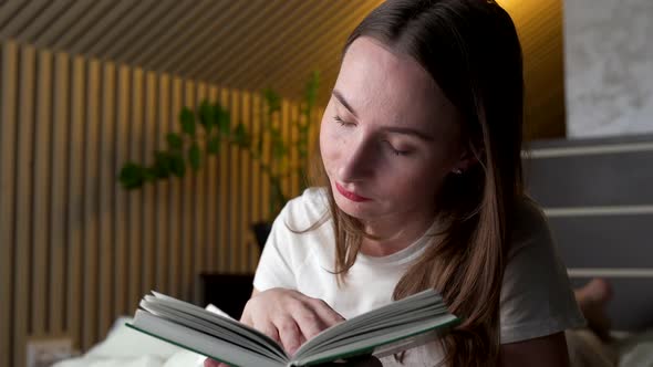 Woman Reads a Book at Home on Her Bed in the Evening