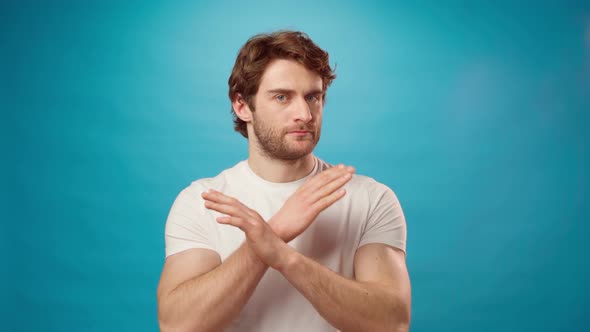 Serious Young Man Says NO with Crossed Hands Against Blue Background