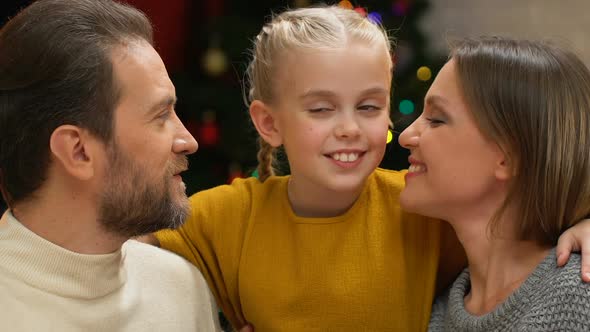 Parents Kissing Daughter, Looking at Camera, Happy Family on Christmas Holiday