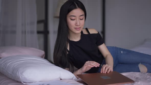 Smiling Asian Woman Closing Laptop Lying Down on Bed Closing Eyes