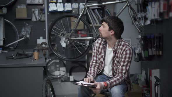 Tired Bike Shop Owner Fills Out Paperwork and Does Calculations for IRS Gets Bored and Drinks Coffee