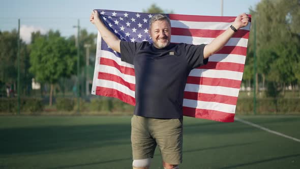 Inspired Happy Amputee with American Flag Looking at Camera Smiling Standing on Summer Sports Field