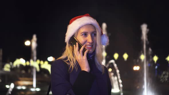 a woman chatting on her smartphone wearing a Santa hat is a night city.