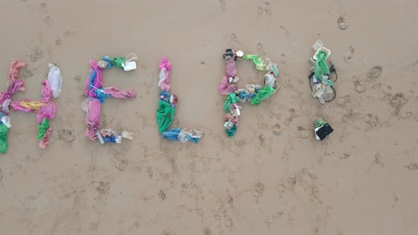 Aerial Shot of a Lettering HELP Made of Trash on a Sandy Beach. A Sad Man Ecological Volunteer Is