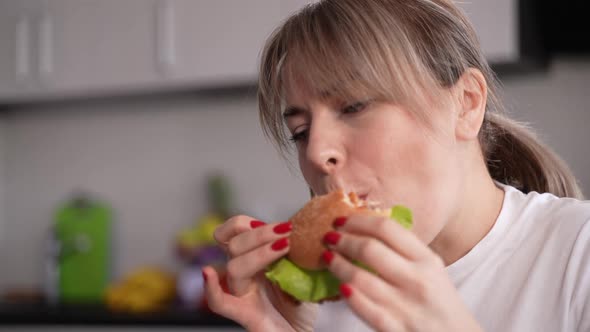 Adult Woman Eating Hamburger at Kitchen Table