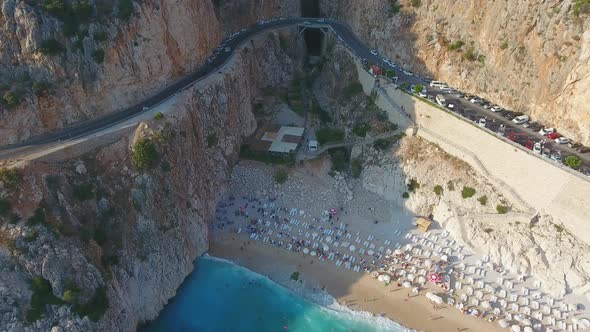 People Swim on Light Blue Sea in the White Sandy Beach Near the Rocky Mountainside