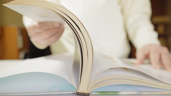 Man Reads a Big Book on a White Table