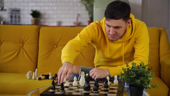 Young Man Sitting on Yellow Sofa and Playing Chess in Room