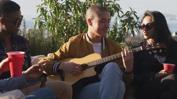 Young man playing guitar on a rooftop with his friends