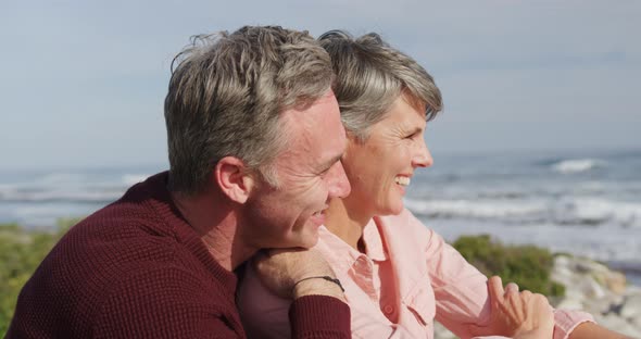 Caucasian couple enjoying free time by sea on a sunny day sitting and embracing