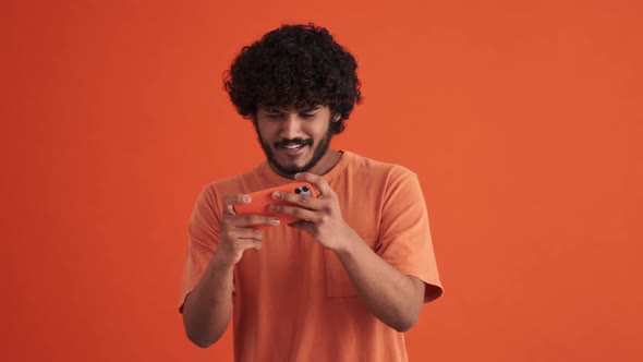 Concentrated curly-haired Indian man playing game by phone and rejoicing about victory