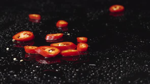 Slices of Red Hot Chili Pepper Falling on Wet Black Surface
