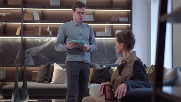 Wide Shot Male Manager Consulting Female Client Sitting on Soft Couch in Furniture Showroom