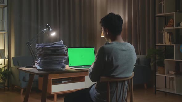 Back View Of Asian Man Having Video Call With Green Screen Laptop While Working With Documents