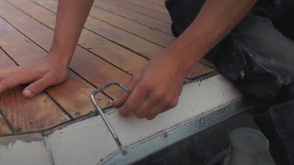 Scraping old mastic sealant between deck planking of wooden boat roof.