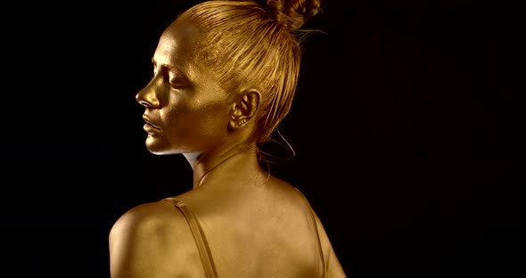 Portrait of a Girl with Golden Glowing Skin on a Black Background. She Closes Her Eyes