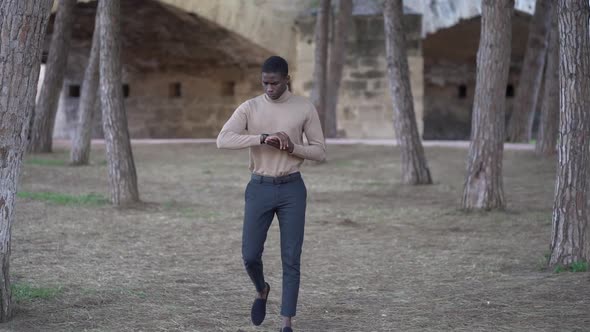 Young man walking in park checking time for appointment