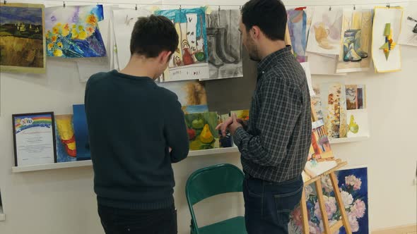 Two Young Men Looking at Paintings in Art Studio