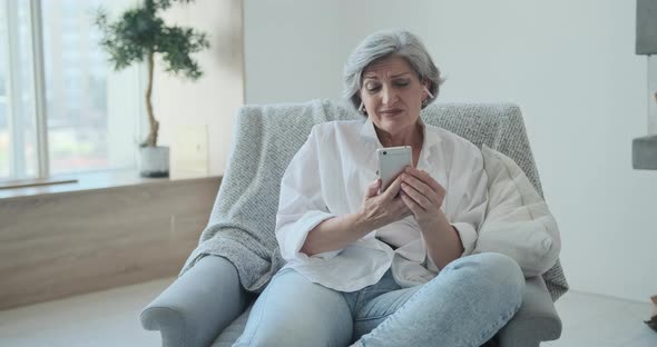 Cheerful Elderly Woman in Earbuds Looking at Her Smartphone Camera Enjoying a Video Call