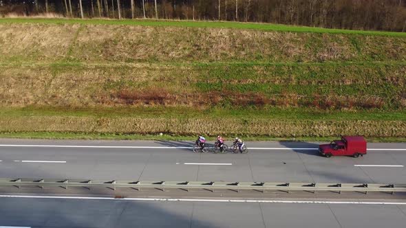 A group of professional athletes cyclists train on a country track, accompanied by a service car.