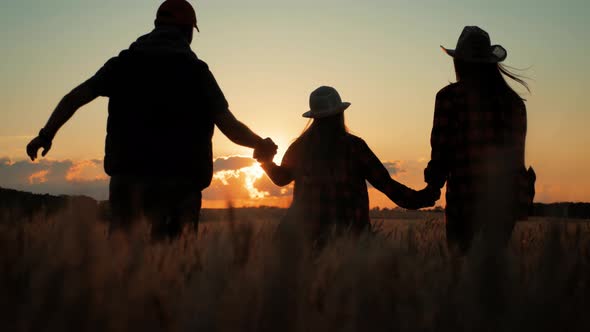 Silhouette Family Farmers Working in a Wheat Field at Sunset. Young Parents with Their Daughter