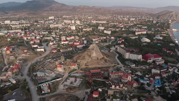 Picturesque Ancient Sudak City with High Stone Hill Among Buildings with Red Roofs on Azure Sea