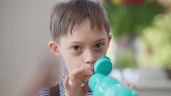 Headshot Portrait of Cute Autistic Boy Drinking Juice Passing Bottle Smiling