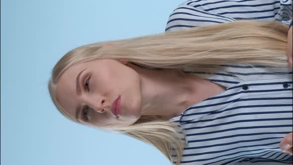 Blonde Young Woman Holding Her Chin with Hand While Thinking About Something on Blue Background.