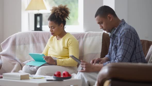 Concentrated African American Woman Messaging Online and Talking to Blurred Man Typing on Laptop