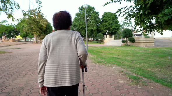 slow-motion of senior woman walking with walking stick in the park