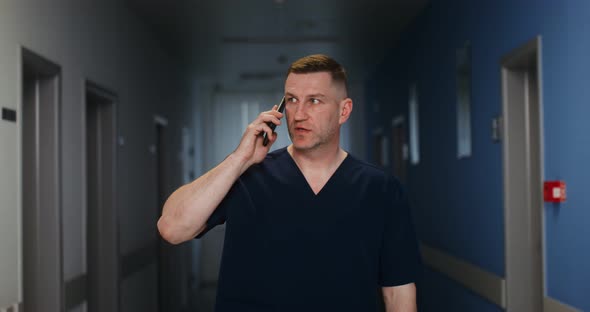 Mature Doctor Talking on a Mobile Phone While Walking Along Hospital Corridor