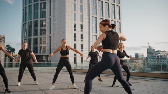 Women Dancing Zumba in the City Square Together with a Young Female Trainer