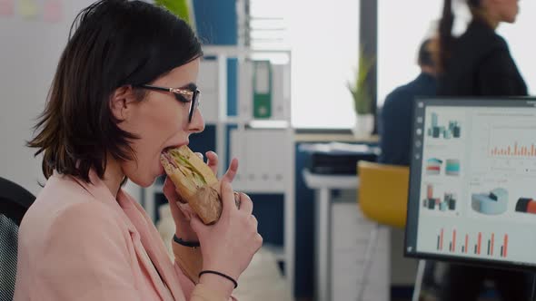 Entrepreneur Woman Eating Tasty Sandwich During Takeout Lunchbreak Working at Financial Graphs