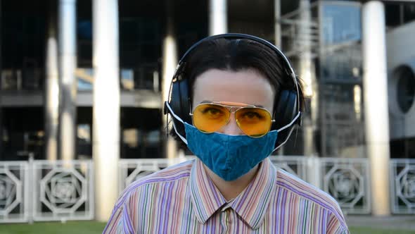 Urban Portrait of a Girl in Big Music Headphones and a Protective Mask