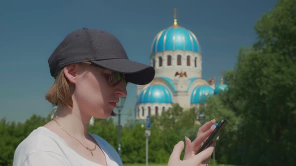 Young Woman Frowns Shakes Head Swipes on Smartphone Church in Background