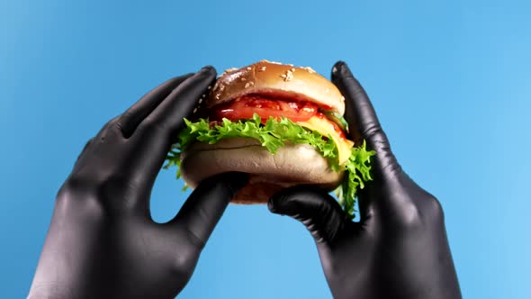 Hands in Black Latex Gloves with Burger on Blue Background