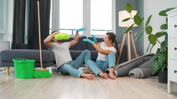 Tired Couple Sits on the Floor in a Room and High Five Each Other After They Finish Cleaning the