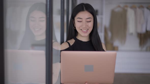 Front View of Smiling Asian Young Woman Waving at Laptop Web Camera Talking