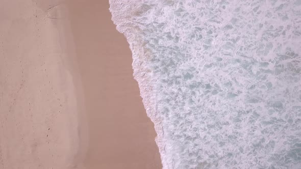 Bird eye view of a man walking on the beach carrying a surfboard. Beautiful drone view of blue waves