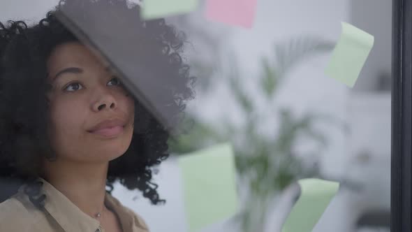 Beautiful African American Businesswoman Sticking Adhesive Notes at Glass Door in Home Office