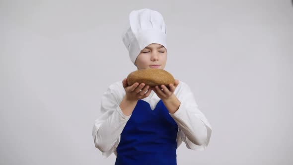 Satisfied Male Little Baker Smelling Delicious Bread Stretching Pastry to Camera Smiling