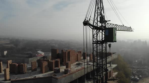 Birds eye view on tower crane in fog standing next to residential building.