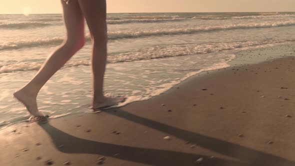 Slender sexy female legs walking on the waves of sea water on a sandy beach.