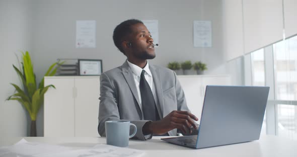 Happy Black Businessman with Headset Having Online Conference on Laptop in Office