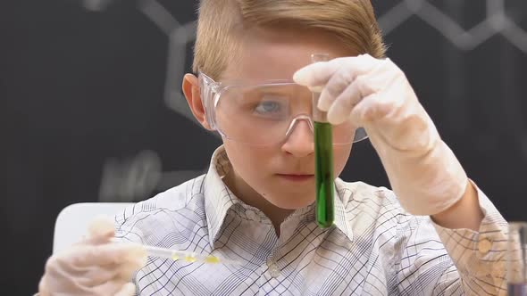 Schoolboy Adding Liquid Into Test Tube With Green Substance, Observing Reaction